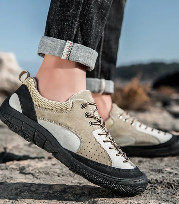 A man in a Tiny Spark brand outfit: a plaid multi-colored jacket, black hoodie, and color-block pants in teal, orange, and purple, sitting on bleachers.